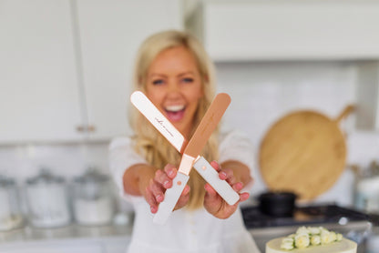 Courtney in her kitchen holding out and crossing her two spatulas in front of her while smiling in the background