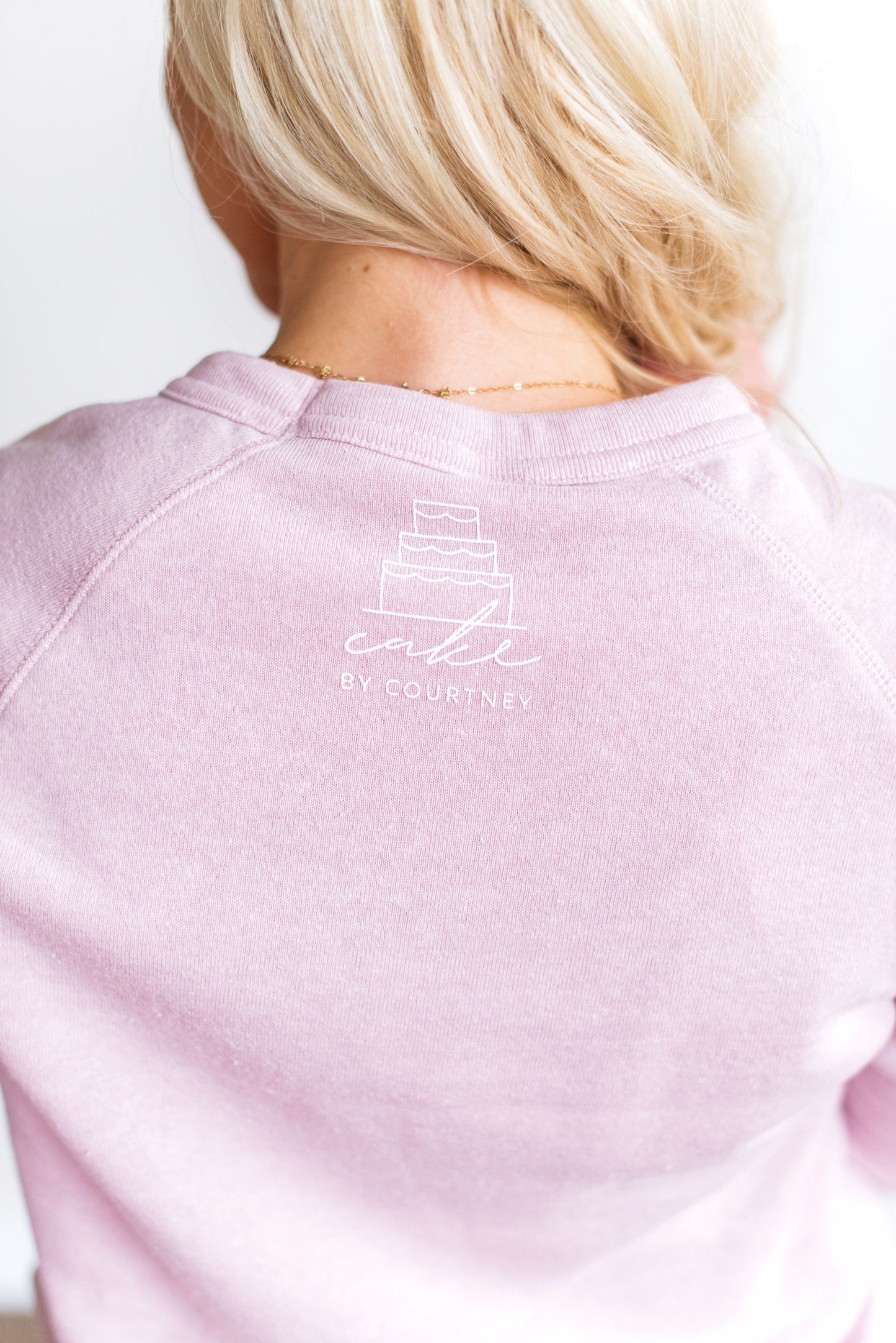 The back of Courtney's light pink 'my good side' sweatshirt showing a close up of Courtneys cake logo at the top of the neck.